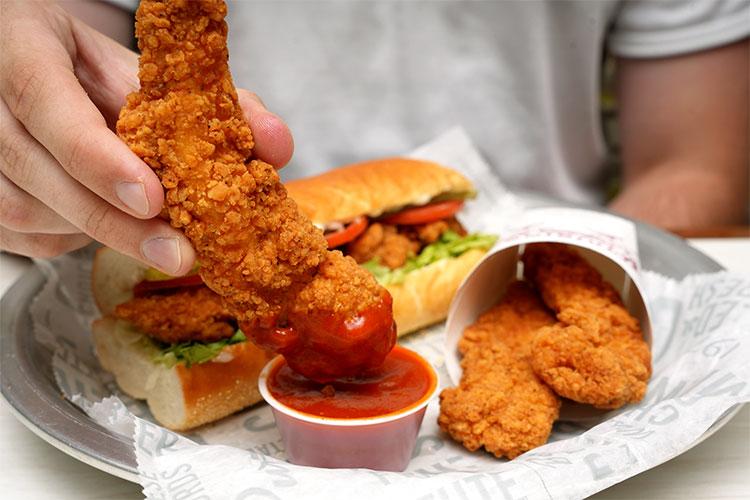 Hand dipping a chicken finger into sauce from Cousins Subs